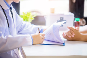 Doctor man consulting patient while filling up an application form at the desk in hospital. Medicine and health care concept